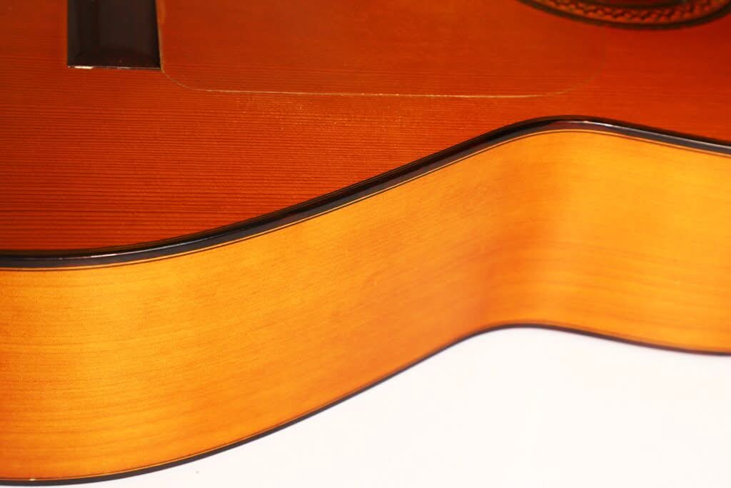 Nahaufnahme der Seite und Oberseite einer Jose Ramirez 1a Flamenco-Gitarre aus dem Jahr 1968, die die glatte, orange-braune Lackierung und die glänzende schwarze Einfassung vor weißem Hintergrund hervorhebt. Nahaufnahme der Seite und Oberseite einer Jose Ramirez 1a Flamenco-Gitarre aus dem Jahr 1968, die die glatte, orange-braune Lackierung und die glänzende schwarze Einfassung vor weißem Hintergrund hervorhebt.
