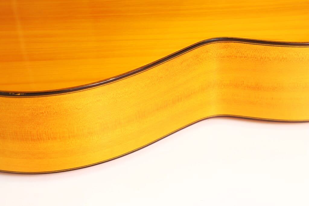 Nahaufnahme der Seite und Oberseite einer Flamenco-Gitarre von Sobrinos de Santos Hernandez aus dem Jahr 1974, die vor weißem Hintergrund die feine Holzmaserung und die elegant geschwungenen Konturen hervorhebt. Nahaufnahme der Seite und Oberseite einer Flamenco-Gitarre von Sobrinos de Santos Hernandez aus dem Jahr 1974, die vor weißem Hintergrund die feine Holzmaserung und die elegant geschwungenen Konturen hervorhebt.