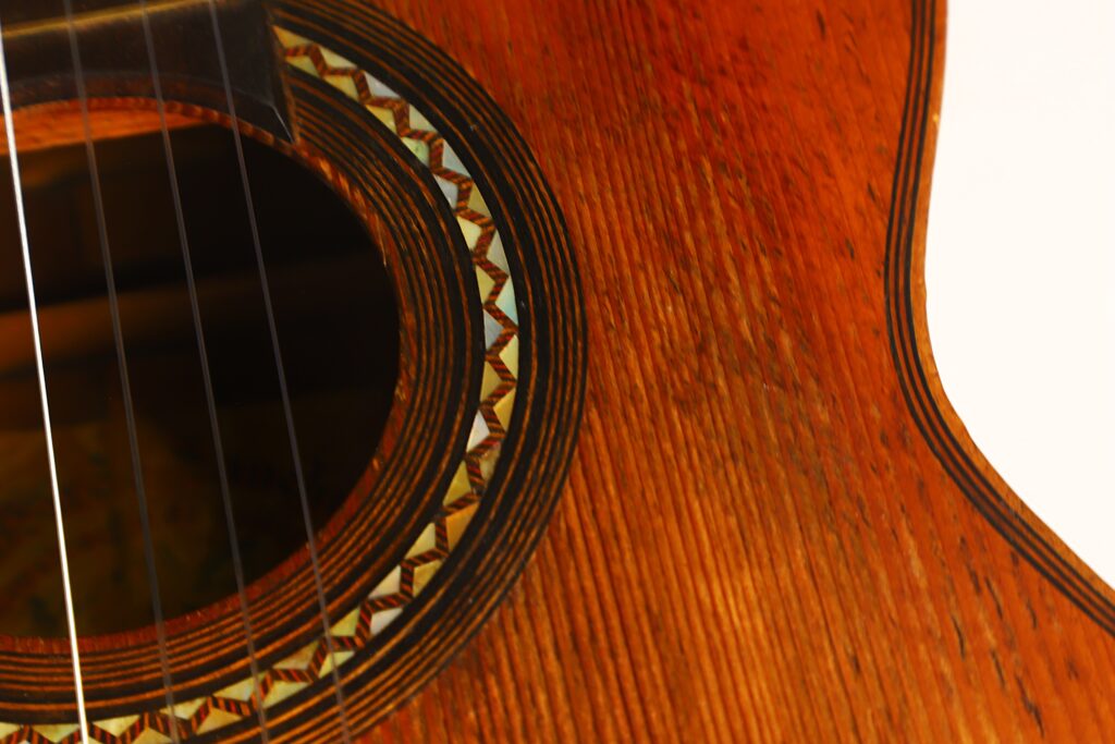 Nahaufnahme des Holzkörpers der „Ricardo Sanchis Nacher 1940 Augustin Barrios Klassische Gitarre“, die das detailreiche Rosettenmuster um das Schallloch sowie die Gitarrensaiten zeigt. Nahaufnahme des Holzkörpers der „Ricardo Sanchis Nacher 1940 Augustin Barrios Klassische Gitarre“, die das detailreiche Rosettenmuster um das Schallloch sowie die Gitarrensaiten zeigt.