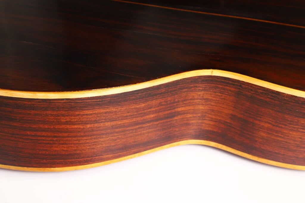 Nahaufnahme der Seite der „Salvador Ibanez 1900 Klassische Gitarre“, die den dunkel polierten Holzkorpus mit helleren Kantenverzierungen vor einem weißen Hintergrund hervorhebt. Nahaufnahme der Seite der „Salvador Ibanez 1900 Klassische Gitarre“, die den dunkel polierten Holzkorpus mit helleren Kantenverzierungen vor einem weißen Hintergrund hervorhebt.