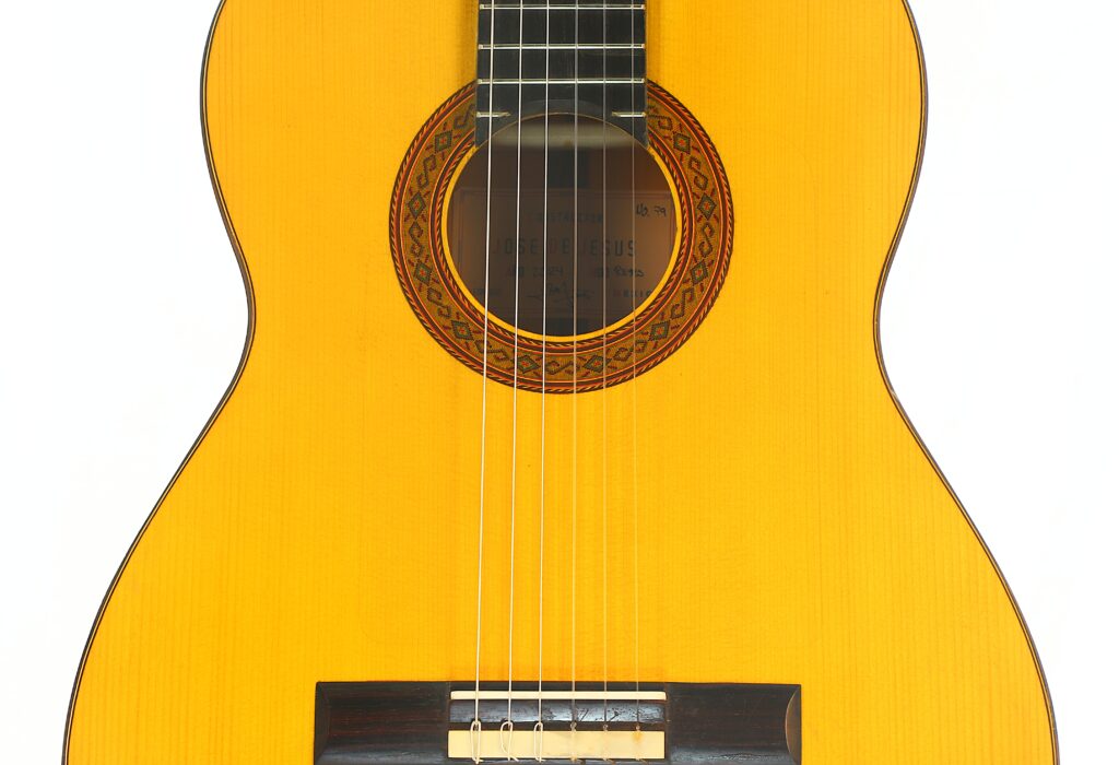 Nahaufnahme der Vorderseite und des Schalllochs der Jose de Jesus 2024 Blanca Modell Reyes Flamenco-Gitarre, die vor einem weißen Hintergrund die sechs Saiten und eine dekorative Rosette zeigt. Nahaufnahme der Vorderseite und des Schalllochs der Jose de Jesus 2024 Blanca Modell Reyes Flamenco-Gitarre, die vor einem weißen Hintergrund die sechs Saiten und eine dekorative Rosette zeigt.