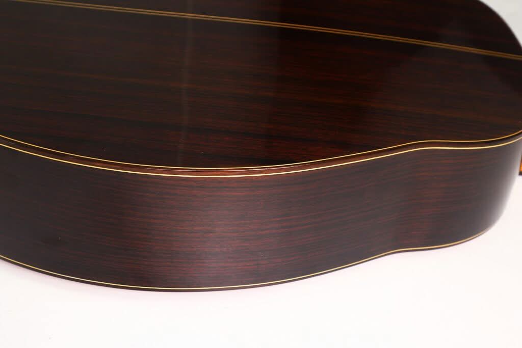 Nahaufnahme der Rückseite und der Seite der „Gran Klassische Gitarre“ von Raimundo y Aparicio Corujo, die das dunkle Holz mit glatter Oberfläche und hellen Zierleisten entlang der Kanten zeigt. Nahaufnahme der Rückseite und der Seite der „Gran Klassische Gitarre“ von Raimundo y Aparicio Corujo, die das dunkle Holz mit glatter Oberfläche und hellen Zierleisten entlang der Kanten zeigt.