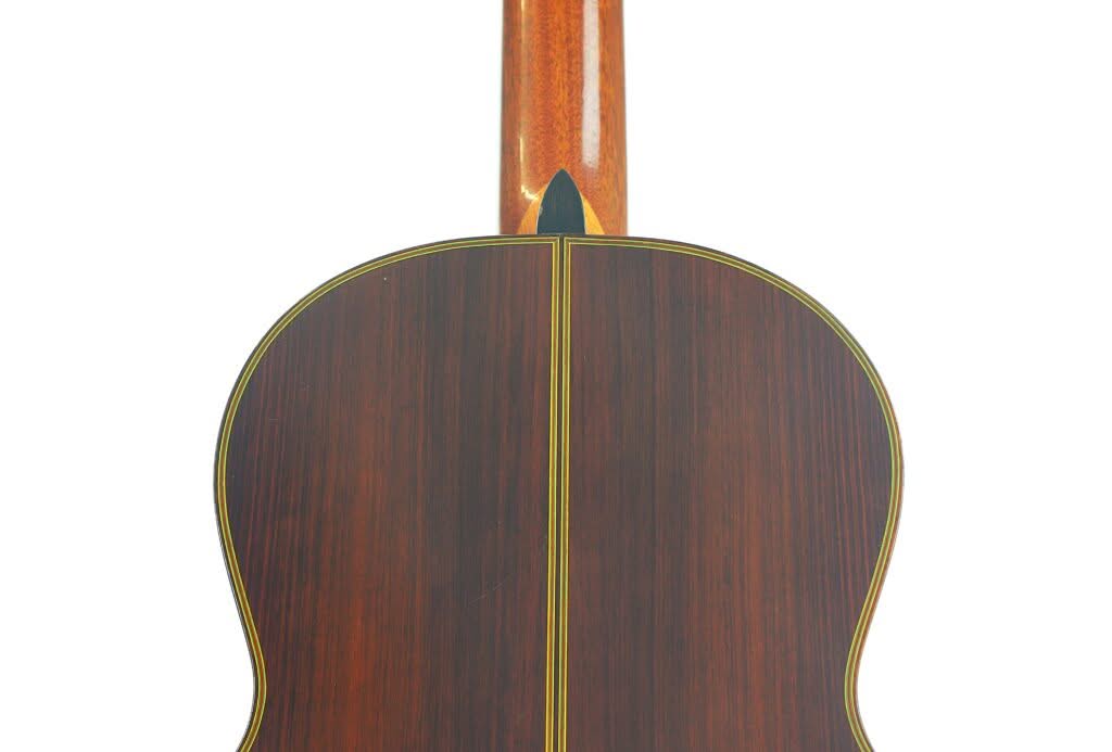 Das Bild zeigt die Rückseite einer „Chet Atkins Klassische Gitarre“ von Juan Estruch aus dem Jahr 1971, die sich durch poliertes dunkles Holz mit einem zentralen gelben Zierstreifen und einem nach oben verlaufenden, glänzenden Hals auszeichnet. Das Bild zeigt die Rückseite einer „Chet Atkins Klassische Gitarre“ von Juan Estruch aus dem Jahr 1971, die sich durch poliertes dunkles Holz mit einem zentralen gelben Zierstreifen und einem nach oben verlaufenden, glänzenden Hals auszeichnet.