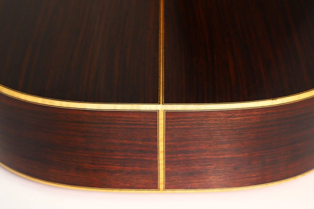 Nahaufnahme der Rückseite und der Seite einer „Hauser Klassische“-Gitarre von Alastair McNeil aus dem Jahr 1997, deren dunkles Holz durch eine helle, cremefarbene Einfassung und einen Mittelstreifen hervorgehoben wird, die die meisterhafte Handwerkskunst des Instrumentes unterstreichen. Nahaufnahme der Rückseite und der Seite einer „Hauser Klassische“-Gitarre von Alastair McNeil aus dem Jahr 1997, deren dunkles Holz durch eine helle, cremefarbene Einfassung und einen Mittelstreifen hervorgehoben wird, die die meisterhafte Handwerkskunst des Instrumentes unterstreichen.