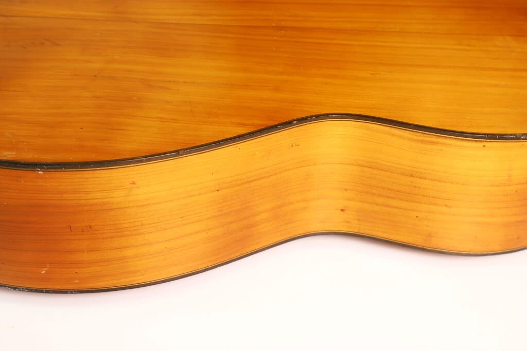 Seitenansicht des Korpus der Flamenco-Gitarre „Manuel de la Chica 1954“ in Nahaufnahme, die die glatte, glänzende Oberfläche und die natürliche Holzmaserung vor weißem Hintergrund hervorhebt. Seitenansicht des Korpus der Flamenco-Gitarre „Manuel de la Chica 1954“ in Nahaufnahme, die die glatte, glänzende Oberfläche und die natürliche Holzmaserung vor weißem Hintergrund hervorhebt.