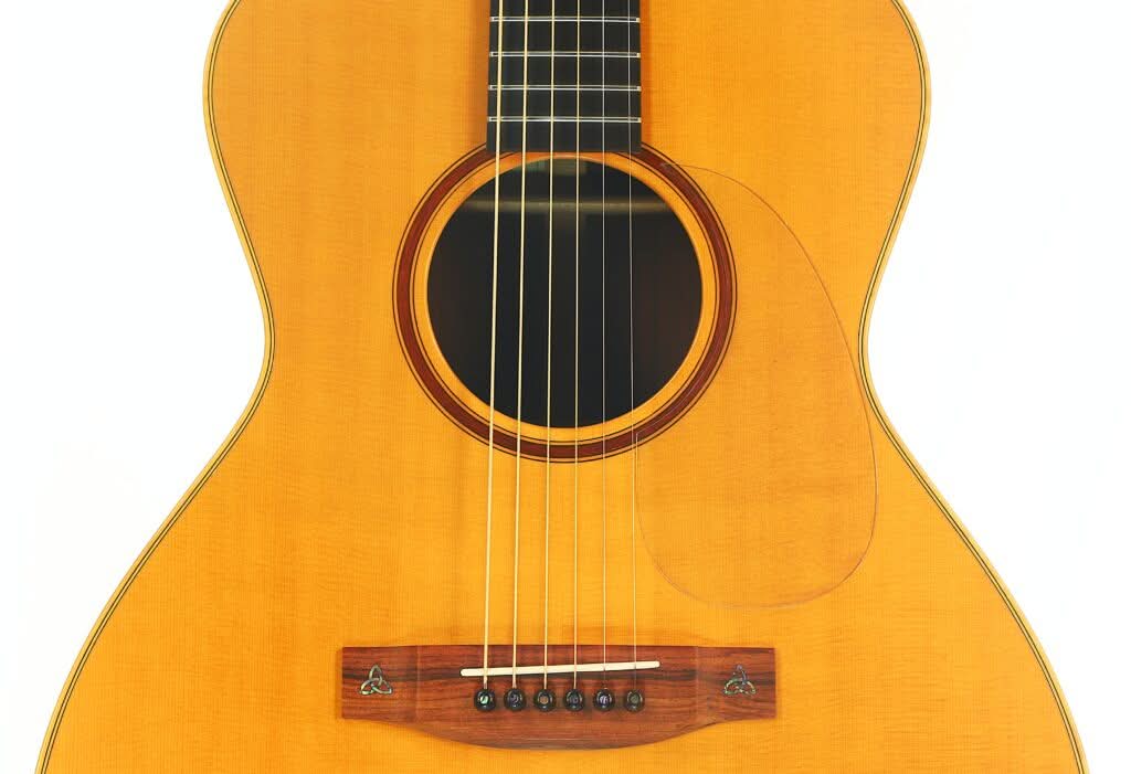 Nahaufnahme des Korpus der Lakewood M-54 Akustikgitarre aus dem Jahr 1998 mit heller Holzoberfläche, rundem Schallloch, sechs Saiten und einem dunklen Steg mit dekorativen Einlagen. Nahaufnahme des Korpus der Lakewood M-54 Akustikgitarre aus dem Jahr 1998 mit heller Holzoberfläche, rundem Schallloch, sechs Saiten und einem dunklen Steg mit dekorativen Einlagen.