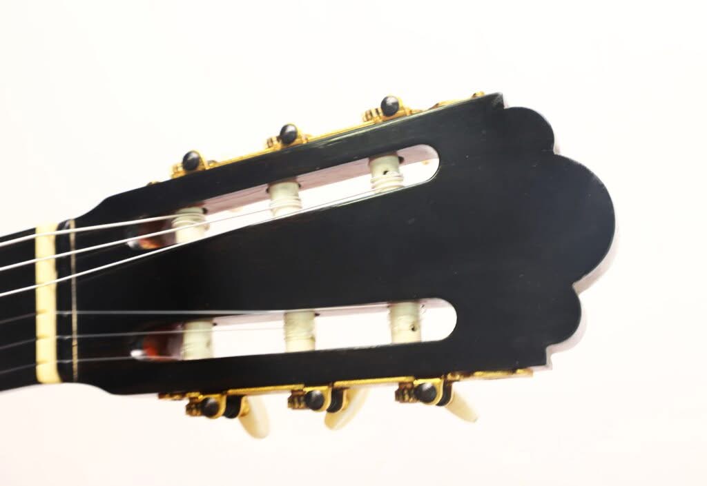 Nahaufnahme des Kopfes einer „Chet Atkins Klassische Gitarre“ von Juan Estruch aus dem Jahr 1971 vor einem schlichten weißen Hintergrund, auf der die Stimmwirbel, die Saiten und ein Teil des Halses zu sehen sind. Nahaufnahme des Kopfes einer „Chet Atkins Klassische Gitarre“ von Juan Estruch aus dem Jahr 1971 vor einem schlichten weißen Hintergrund, auf der die Stimmwirbel, die Saiten und ein Teil des Halses zu sehen sind.