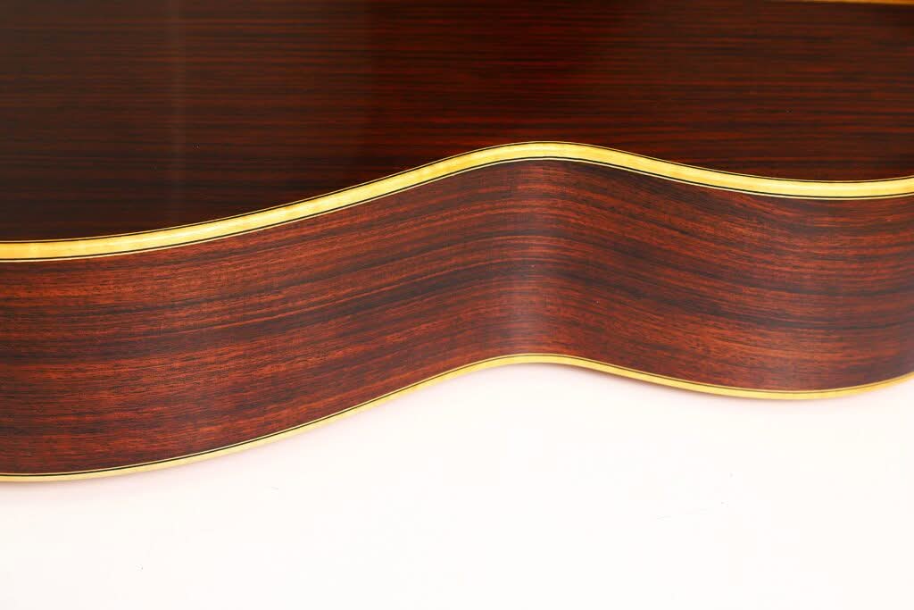 Nahaufnahme der Seite der „Alastair McNeil 1997 Hauser Klassische Gitarre“, die eine dunkle Holzmaserung mit einer sanften Wölbung und einer gelben Einfassung entlang der Kante zeigt, vor einem weißen Hintergrund. Nahaufnahme der Seite der „Alastair McNeil 1997 Hauser Klassische Gitarre“, die eine dunkle Holzmaserung mit einer sanften Wölbung und einer gelben Einfassung entlang der Kante zeigt, vor einem weißen Hintergrund.