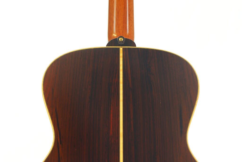 Das Bild zeigt die Rückseite einer Lakewood M-54 Akustikgitarre aus dem Jahr 1998, die sich durch dunkles Holz mit einem hellen, vertikalen Einlegeband in der Mitte und hellen Kanten auszeichnet. Oben ist der Gitarrenhals zu sehen. Das Bild zeigt die Rückseite einer Lakewood M-54 Akustikgitarre aus dem Jahr 1998, die sich durch dunkles Holz mit einem hellen, vertikalen Einlegeband in der Mitte und hellen Kanten auszeichnet. Oben ist der Gitarrenhals zu sehen.