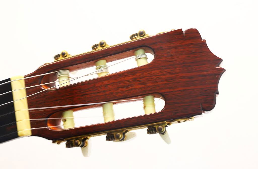 Nahaufnahme des Kopfes der „Klassische Gitarre“ von Antonio Duran aus dem Jahr 1974 mit Holzoberfläche, goldenen Stimmwirbeln und Nylonsaiten vor weißem Hintergrund. Nahaufnahme des Kopfes der „Klassische Gitarre“ von Antonio Duran aus dem Jahr 1974 mit Holzoberfläche, goldenen Stimmwirbeln und Nylonsaiten vor weißem Hintergrund.