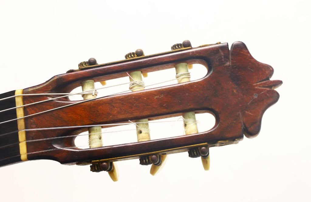 Nahaufnahme der Kopfplatte einer Modesto-Borreguero-Gitarre aus dem Jahr 1955 mit hölzernen Stimmwirbeln und umsponnenen Saiten vor einem schlichten weißen Hintergrund. Nahaufnahme der Kopfplatte einer Modesto-Borreguero-Gitarre aus dem Jahr 1955 mit hölzernen Stimmwirbeln und umsponnenen Saiten vor einem schlichten weißen Hintergrund.