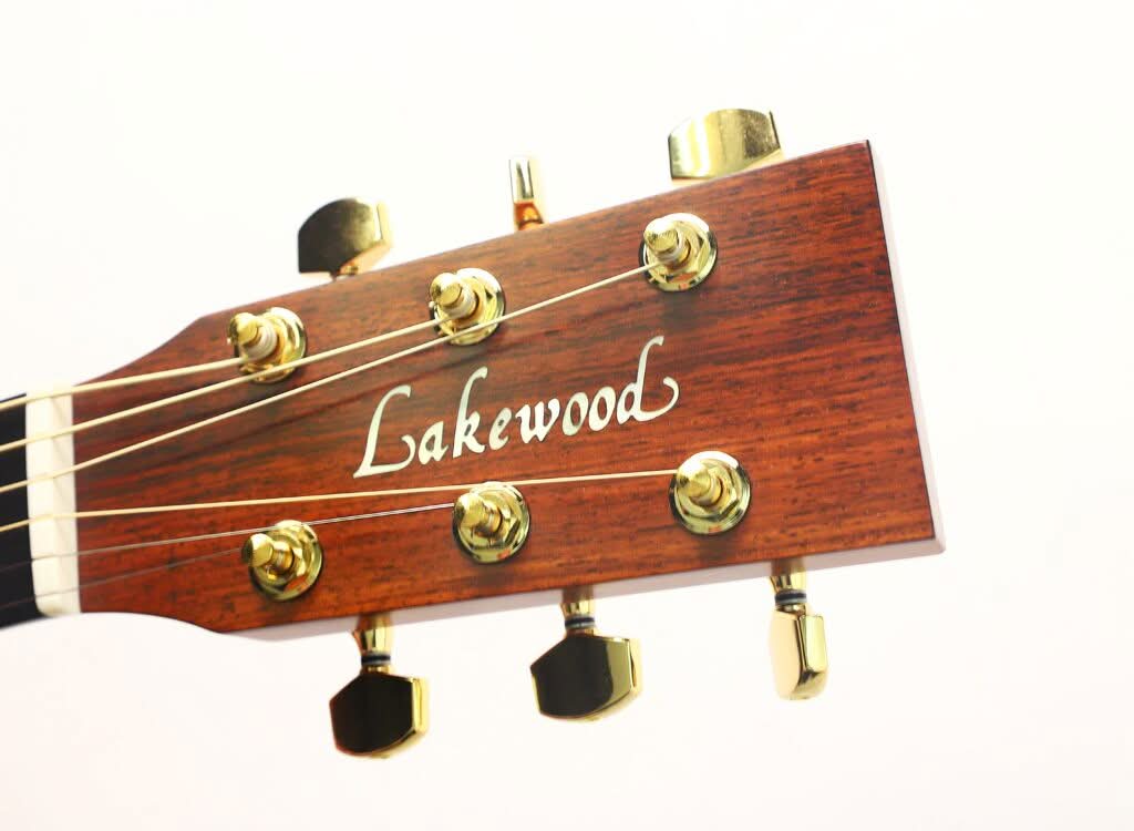 Nahaufnahme des Kopfes einer Lakewood M-54 Akustikgitarre aus dem Jahr 1998 mit sechs goldenen Stimmwirbeln und dem weißen Lakewood-Logo auf Holz vor einem schlichten weißen Hintergrund. Nahaufnahme des Kopfes einer Lakewood M-54 Akustikgitarre aus dem Jahr 1998 mit sechs goldenen Stimmwirbeln und dem weißen Lakewood-Logo auf Holz vor einem schlichten weißen Hintergrund.