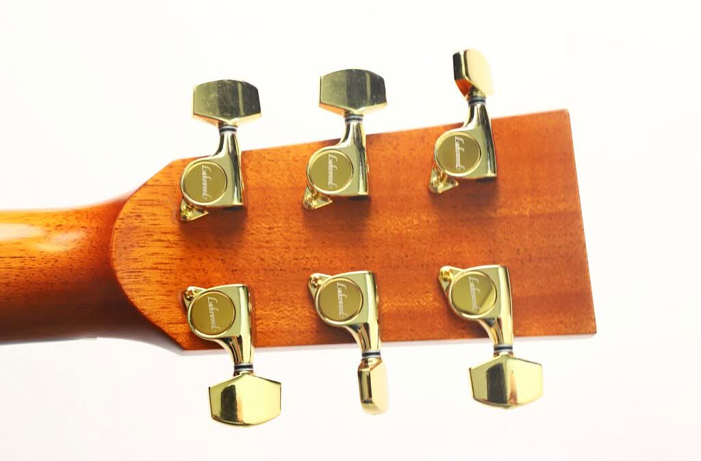 Nahaufnahme der Rückseite des Kopfes einer Lakewood M-54 Akustikgitarre aus dem Jahr 1998 mit sechs glänzenden goldenen Stimmwirbeln auf einem Holzfinish, vor einem schlichten weißen Hintergrund. Nahaufnahme der Rückseite des Kopfes einer Lakewood M-54 Akustikgitarre aus dem Jahr 1998 mit sechs glänzenden goldenen Stimmwirbeln auf einem Holzfinish, vor einem schlichten weißen Hintergrund.