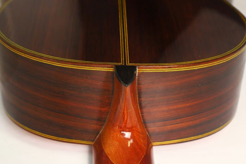 Nahaufnahme des Halsansatzes der „Chet Atkins Klassische Gitarre“ von Juan Estruch aus dem Jahr 1971, die sich durch poliertes dunkles Holz mit sichtbarer Maserung, gelbe Akzente und meisterhafte Handwerkskunst auszeichnet. Nahaufnahme des Halsansatzes der „Chet Atkins Klassische Gitarre“ von Juan Estruch aus dem Jahr 1971, die sich durch poliertes dunkles Holz mit sichtbarer Maserung, gelbe Akzente und meisterhafte Handwerkskunst auszeichnet.