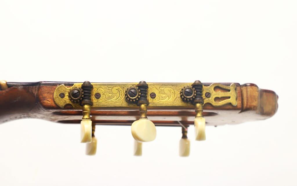 Nahaufnahme der Seite des Kopfes einer Modesto-Borreguero-Gitarre aus dem Jahr 1955, auf der drei kunstvoll verzierte goldene Stimmwirbel mit Elfenbeinknöpfen vor weißem Hintergrund zu sehen sind. Nahaufnahme der Seite des Kopfes einer Modesto-Borreguero-Gitarre aus dem Jahr 1955, auf der drei kunstvoll verzierte goldene Stimmwirbel mit Elfenbeinknöpfen vor weißem Hintergrund zu sehen sind.