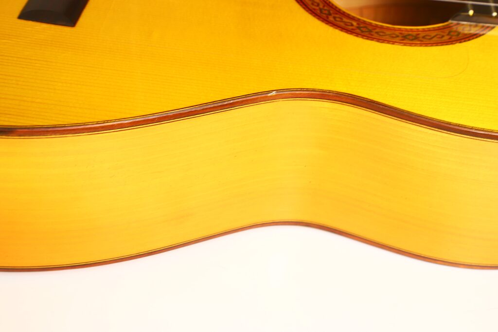 Nahaufnahme des Korpus der Flamenco-Gitarre „Jose de Jesus 2024 Blanca Modell Reyes“ aus gelblich schimmerndem Holz mit sichtbarer Maserung und Zierkante, fotografiert vor weißem Hintergrund. Nahaufnahme des Korpus der Flamenco-Gitarre „Jose de Jesus 2024 Blanca Modell Reyes“ aus gelblich schimmerndem Holz mit sichtbarer Maserung und Zierkante, fotografiert vor weißem Hintergrund.