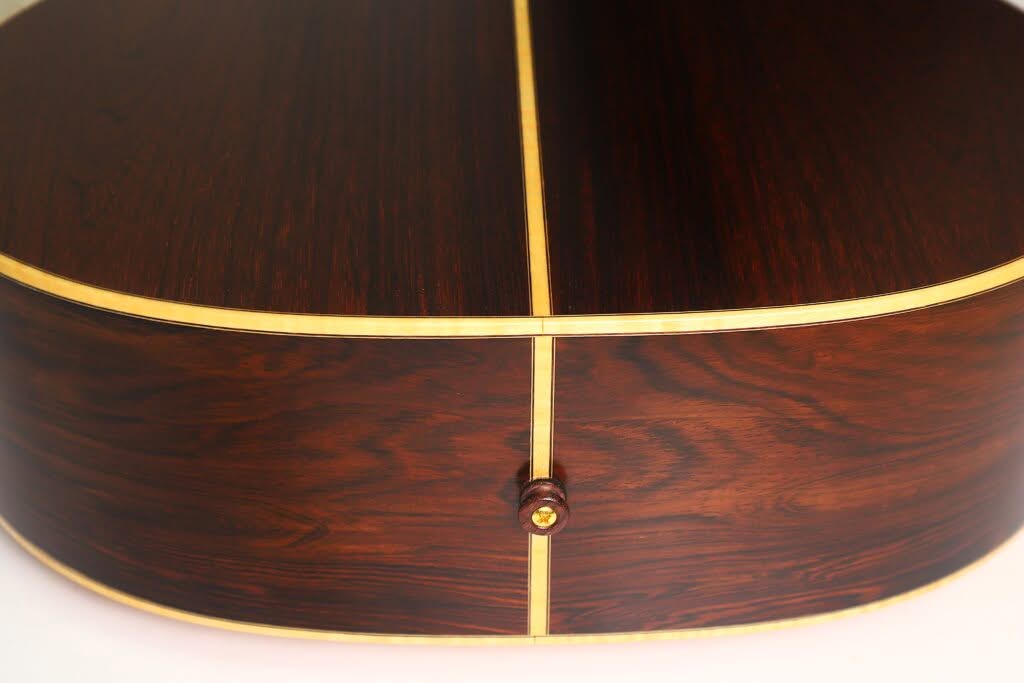 Nahaufnahme der Rückseite und der Seite einer Lakewood M-54 Akustikgitarre aus dem Jahr 1998, die die satte, dunkle Holzmaserung, den hellen Einlegestreifen und einen Gurtknopf nahe der Unterkante hervorhebt. Nahaufnahme der Rückseite und der Seite einer Lakewood M-54 Akustikgitarre aus dem Jahr 1998, die die satte, dunkle Holzmaserung, den hellen Einlegestreifen und einen Gurtknopf nahe der Unterkante hervorhebt.