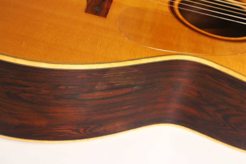 Nahaufnahme des Korpus der Lakewood M-54 Akustikgitarre aus dem Jahr 1998, die die Holzmaserung an den Zargen und der Decke hervorhebt; in der oberen rechten Ecke sind die Saiten und ein Teil des Schalllochs teilweise zu sehen. Nahaufnahme des Korpus der Lakewood M-54 Akustikgitarre aus dem Jahr 1998, die die Holzmaserung an den Zargen und der Decke hervorhebt; in der oberen rechten Ecke sind die Saiten und ein Teil des Schalllochs teilweise zu sehen.