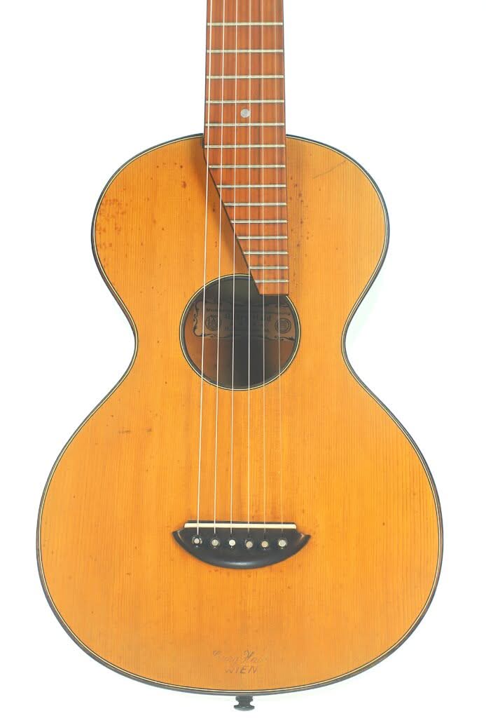 Die Georg Haid 1936 Terz-Gitarre ist eine Vintage-Akustikgitarre mit einem Korpus aus hellem Holz, einem runden Schallloch, sechs Saiten sowie einem schlichten schwarzen Steg und Griffbrett. Die Georg Haid 1936 Terz-Gitarre ist eine Vintage-Akustikgitarre mit einem Korpus aus hellem Holz, einem runden Schallloch, sechs Saiten sowie einem schlichten schwarzen Steg und Griffbrett.
