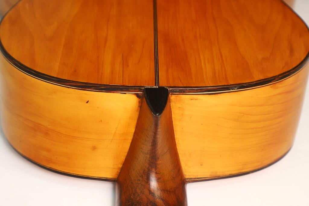 Nahaufnahme des Rückenteils der Akustikgitarre „Modesto Borreguero 1955“, die die glatte, polierte Holzmaserung und den detailreichen Halsansatz an der Verbindungsstelle zwischen Hals und Korpus zeigt. Nahaufnahme des Rückenteils der Akustikgitarre „Modesto Borreguero 1955“, die die glatte, polierte Holzmaserung und den detailreichen Halsansatz an der Verbindungsstelle zwischen Hals und Korpus zeigt.