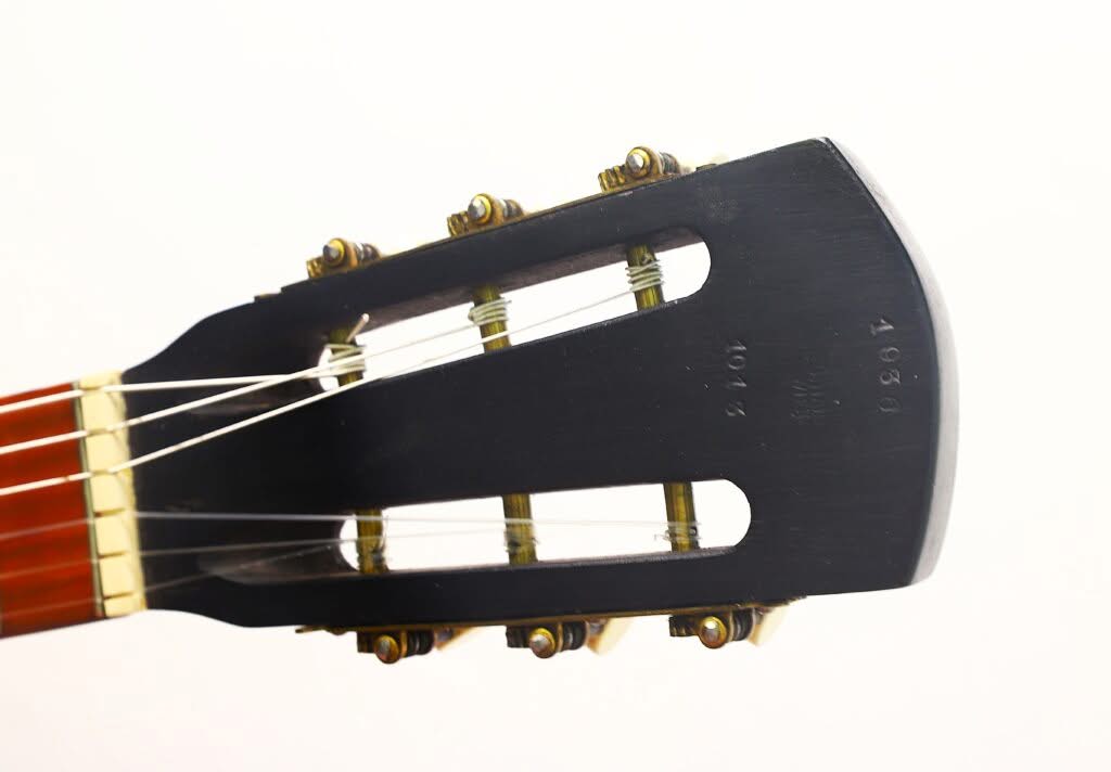 Nahaufnahme des Kopfes einer Georg-Haid-Terz-Gitarre aus dem Jahr 1936 mit sechs Stimmwirbeln, Messingbeschlägen, Nylonsaiten und sichtbaren Seriennummern auf dunklem Holz vor einem schlichten weißen Hintergrund. Nahaufnahme des Kopfes einer Georg-Haid-Terz-Gitarre aus dem Jahr 1936 mit sechs Stimmwirbeln, Messingbeschlägen, Nylonsaiten und sichtbaren Seriennummern auf dunklem Holz vor einem schlichten weißen Hintergrund.