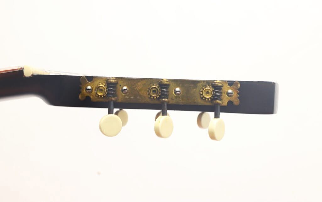 Nahaufnahme der Seite des Kopfes einer Terz-Gitarre von Georg Haid aus dem Jahr 1936, auf der drei weiße Stimmwirbel und Messing-Stimmmechaniken vor einem schlichten weißen Hintergrund zu sehen sind. Nahaufnahme der Seite des Kopfes einer Terz-Gitarre von Georg Haid aus dem Jahr 1936, auf der drei weiße Stimmwirbel und Messing-Stimmmechaniken vor einem schlichten weißen Hintergrund zu sehen sind.