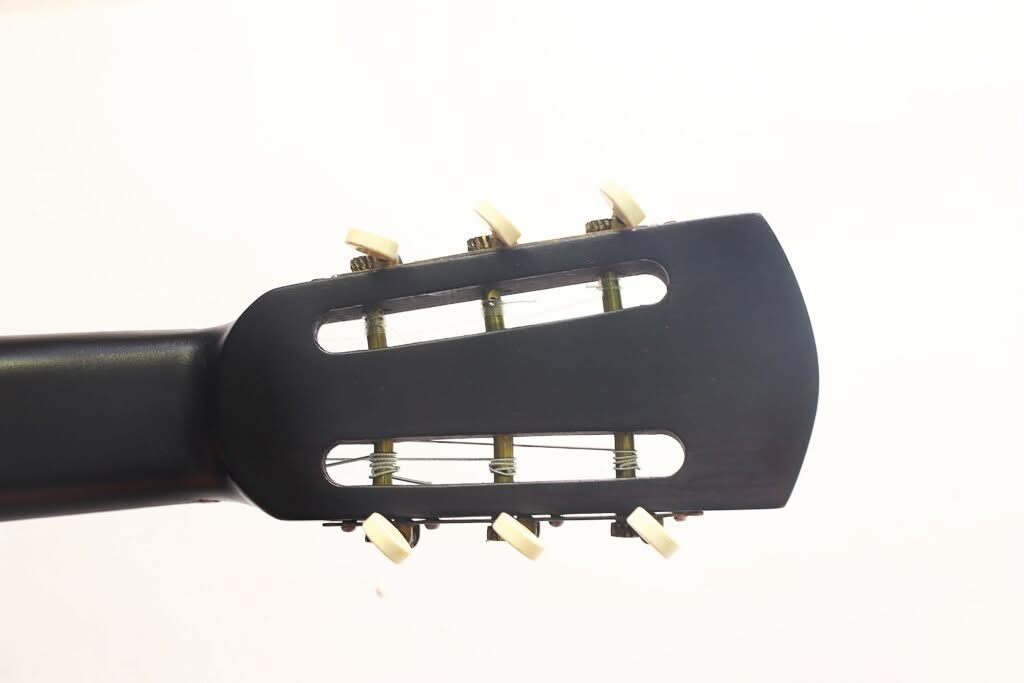 Nahaufnahme des schwarzen Kopfes der Georg-Haid-Terz-Gitarre von 1936 mit sechs weißen Stimmwirbeln und Nylonsaiten vor einem schlichten weißen Hintergrund. Nahaufnahme des schwarzen Kopfes der Georg-Haid-Terz-Gitarre von 1936 mit sechs weißen Stimmwirbeln und Nylonsaiten vor einem schlichten weißen Hintergrund.
