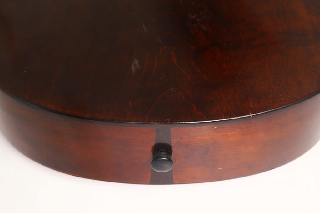 Nahaufnahme der Georg-Haid-Terz-Gitarre von 1936 mit einem runden Korpus aus dunklem Holz, einer glatten, polierten Oberfläche und einem kleinen schwarzen Drehknopf an der Seite, vor weißem Hintergrund. Nahaufnahme der Georg-Haid-Terz-Gitarre von 1936 mit einem runden Korpus aus dunklem Holz, einer glatten, polierten Oberfläche und einem kleinen schwarzen Drehknopf an der Seite, vor weißem Hintergrund.