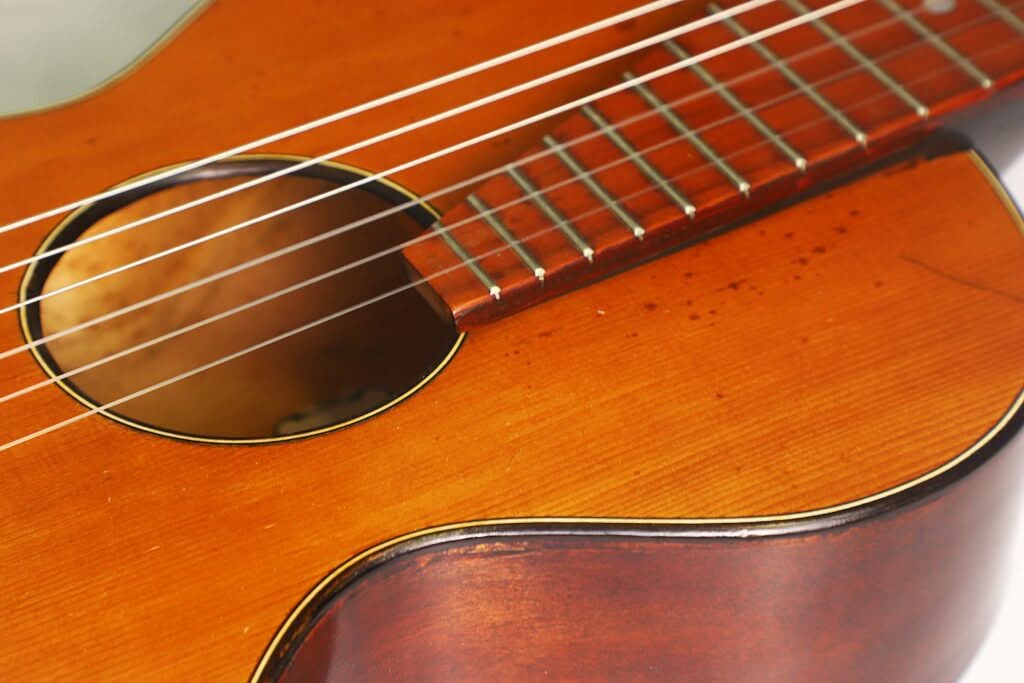 Nahaufnahme der Georg-Haid-Terz-Gitarre von 1936, die die Saiten, das Schallloch sowie einen Ausschnitt des polierten Holzgriffbretts und des Korpus zeigt. Nahaufnahme der Georg-Haid-Terz-Gitarre von 1936, die die Saiten, das Schallloch sowie einen Ausschnitt des polierten Holzgriffbretts und des Korpus zeigt.