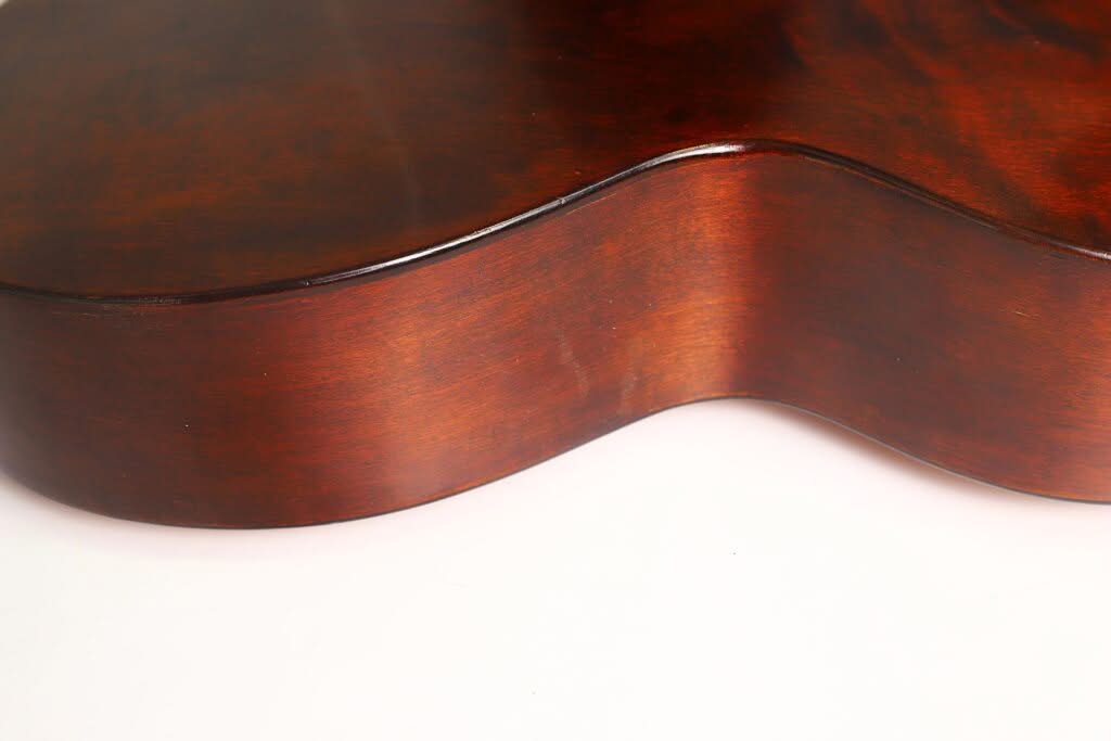 Nahaufnahme der Seite und Rückseite der Georg-Haid-Terz-Gitarre von 1936 vor weißem Hintergrund, die ihre sanften Rundungen und die satte, braune, polierte Holzoberfläche hervorhebt. Nahaufnahme der Seite und Rückseite der Georg-Haid-Terz-Gitarre von 1936 vor weißem Hintergrund, die ihre sanften Rundungen und die satte, braune, polierte Holzoberfläche hervorhebt.