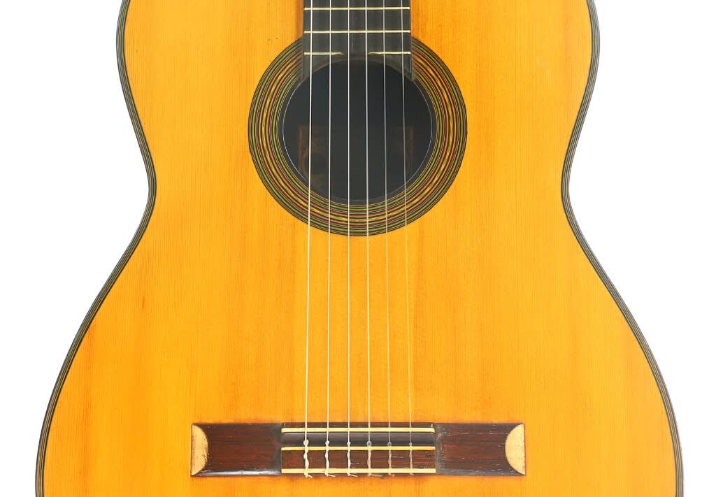Nahaufnahme der „Francisco Simplicio 1931 Torres Klassische Gitarre“, bei der die sechs Saiten, das Schallloch und der Holzsteg vor weißem Hintergrund hervorgehoben sind. Nahaufnahme der „Francisco Simplicio 1931 Torres Klassische Gitarre“, bei der die sechs Saiten, das Schallloch und der Holzsteg vor weißem Hintergrund hervorgehoben sind.