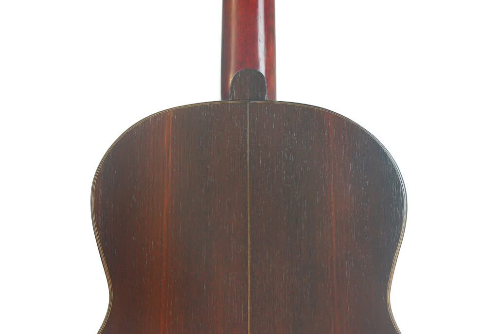 Rückansicht der „Francisco Simplicio 1931 Torres Klassische Gitarre“, die den Korpus der Akustikgitarre aus dunklem Holz mit einer Mittelnaht hervorhebt, vor weißem Hintergrund. Rückansicht der „Francisco Simplicio 1931 Torres Klassische Gitarre“, die den Korpus der Akustikgitarre aus dunklem Holz mit einer Mittelnaht hervorhebt, vor weißem Hintergrund.