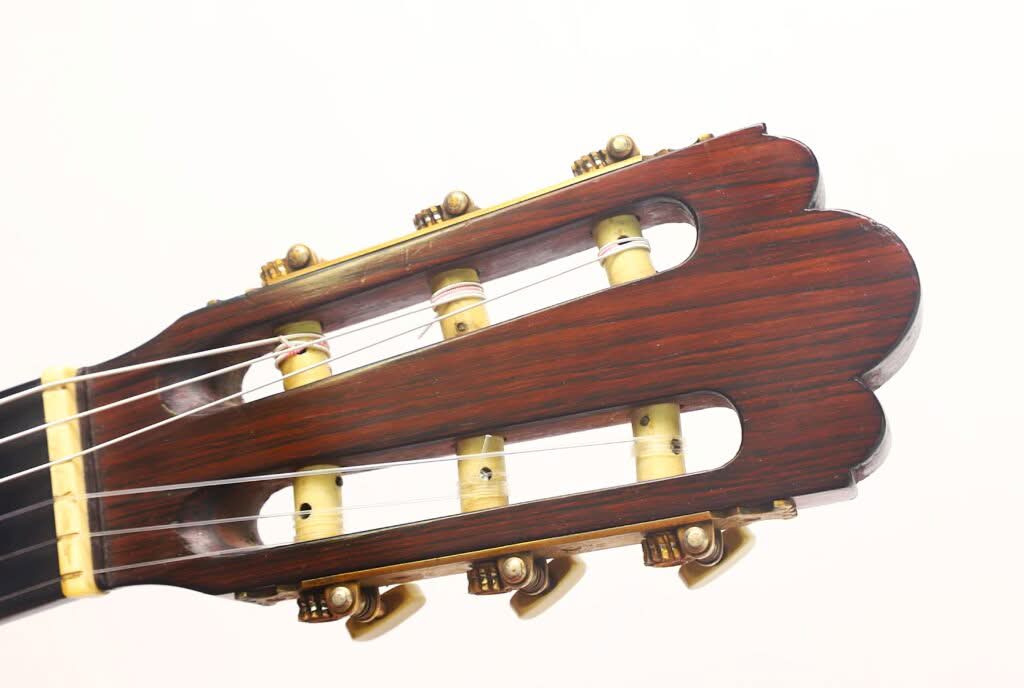 Nahaufnahme des Kopfes einer „Torres Klassische Gitarre“ von Francisco Simplicio aus dem Jahr 1931 mit sechs Stimmwirbeln und Saiten aus dunkel poliertem Holz vor einem schlichten weißen Hintergrund. Nahaufnahme des Kopfes einer „Torres Klassische Gitarre“ von Francisco Simplicio aus dem Jahr 1931 mit sechs Stimmwirbeln und Saiten aus dunkel poliertem Holz vor einem schlichten weißen Hintergrund.