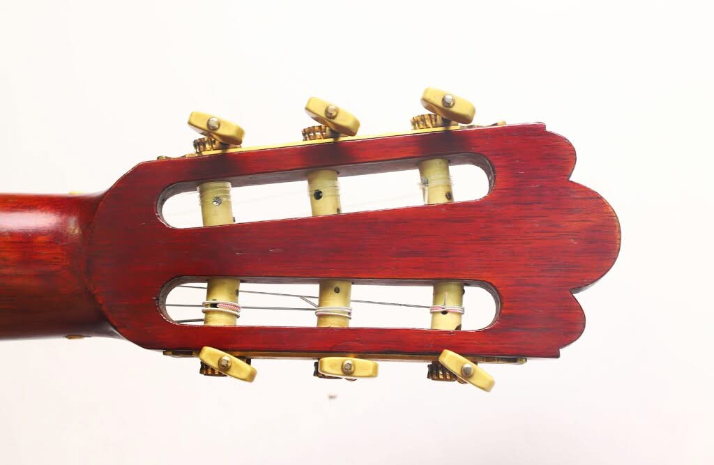 Nahaufnahme des hölzernen Kopfstücks der „Francisco Simplicio 1931 Torres Klassische Gitarre“ mit sechs Stimmwirbeln und Saiten vor einem schlichten weißen Hintergrund. Nahaufnahme des hölzernen Kopfstücks der „Francisco Simplicio 1931 Torres Klassische Gitarre“ mit sechs Stimmwirbeln und Saiten vor einem schlichten weißen Hintergrund.