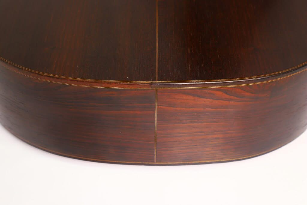 Nahaufnahme der Rückseite und der Seite der „Francisco Simplicio 1931 Torres Klassische Gitarre“, die das dunkle, polierte Holz, die glatte Maserung und die feine Fuge an der Verbindungsstelle der beiden Teile vor einem weißen Hintergrund hervorhebt. Nahaufnahme der Rückseite und der Seite der „Francisco Simplicio 1931 Torres Klassische Gitarre“, die das dunkle, polierte Holz, die glatte Maserung und die feine Fuge an der Verbindungsstelle der beiden Teile vor einem weißen Hintergrund hervorhebt.