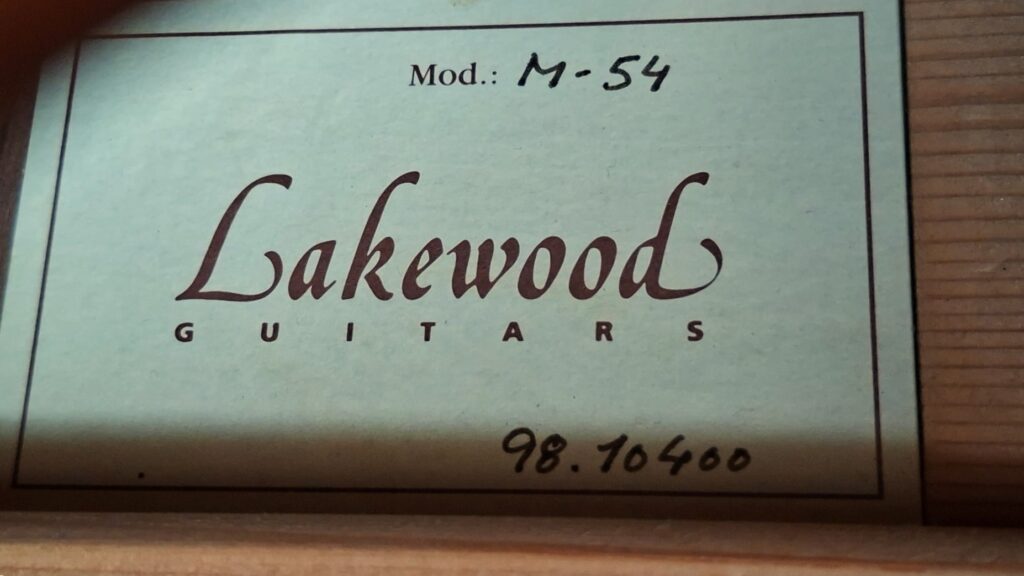 Auf einem Etikett im Inneren der Gitarre steht „Lakewood Guitars“. Das Modell ist handschriftlich mit „M-54“ angegeben, und die Seriennummer 98.10400 befindet sich unten auf der Holzmaserung. Produkt: Lakewood M-54 1998 Akustikgitarre. Auf einem Etikett im Inneren der Gitarre steht „Lakewood Guitars“. Das Modell ist handschriftlich mit „M-54“ angegeben, und die Seriennummer 98.10400 befindet sich unten auf der Holzmaserung. Produkt: Lakewood M-54 1998 Akustikgitarre.