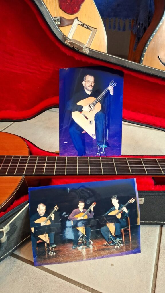 Eine „Gran Klassische Gitarre“ von Raimundo y Aparicio Corujo in ihrem Koffer, dazu zwei gedruckte Fotos: eines zeigt einen Mann, der eine ähnliche Gitarre in der Hand hält, und das andere drei Personen, die auf einer Bühne sitzen und Gitarre spielen. Eine „Gran Klassische Gitarre“ von Raimundo y Aparicio Corujo in ihrem Koffer, dazu zwei gedruckte Fotos: eines zeigt einen Mann, der eine ähnliche Gitarre in der Hand hält, und das andere drei Personen, die auf einer Bühne sitzen und Gitarre spielen.