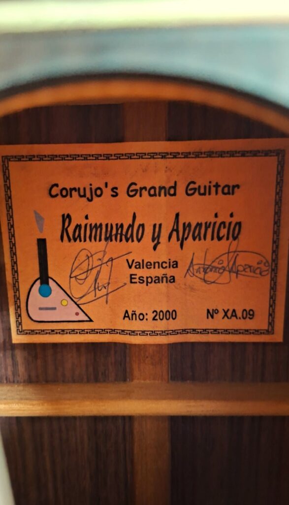 Auf dem orangefarbenen Etikett im Inneren der Gitarre steht „Raimundo y Aparicio Corujo’s Gran Klassische Gitarre, Valencia España, Año: 2000, Nº XA.09“; es trägt zwei Unterschriften und ist von einem schwarzen, gemusterten Rahmen umgeben. Auf dem orangefarbenen Etikett im Inneren der Gitarre steht „Raimundo y Aparicio Corujo’s Gran Klassische Gitarre, Valencia España, Año: 2000, Nº XA.09“; es trägt zwei Unterschriften und ist von einem schwarzen, gemusterten Rahmen umgeben.