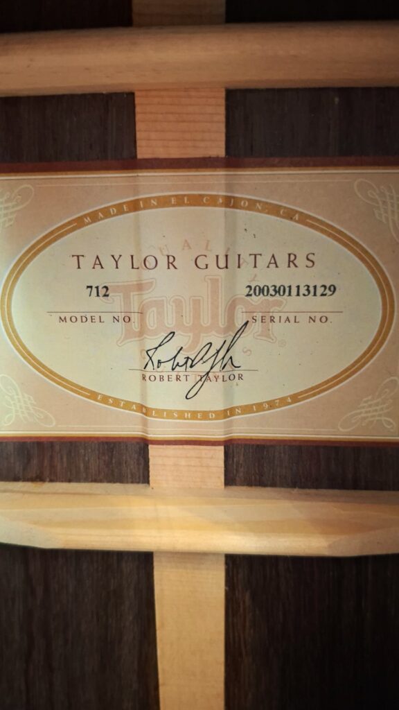 Nahaufnahme eines Etiketts der Taylor 712 Akustikgitarre im Inneren des Instruments, auf dem die Modellnummer 712, die Seriennummer 20030131329 und eine Unterschrift von Robert Taylor zu sehen sind. Nahaufnahme eines Etiketts der Taylor 712 Akustikgitarre im Inneren des Instruments, auf dem die Modellnummer 712, die Seriennummer 20030131329 und eine Unterschrift von Robert Taylor zu sehen sind.