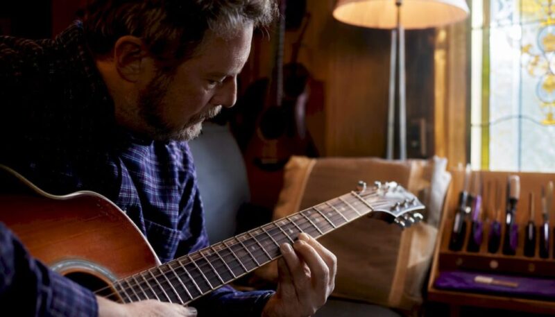 Man inspecting guitar fret wear under lamp