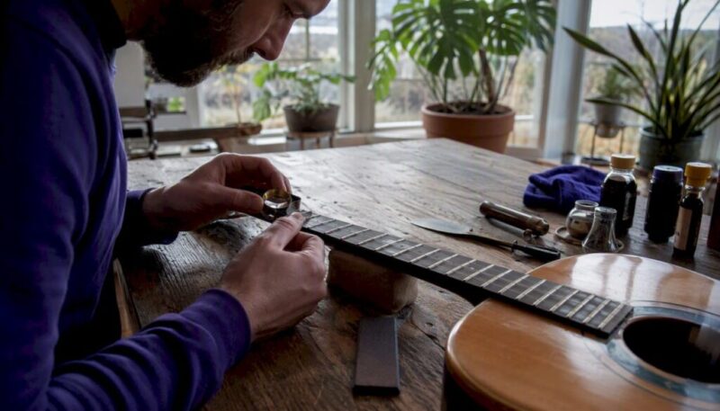 Hands inspecting guitar fretboard with magnifier