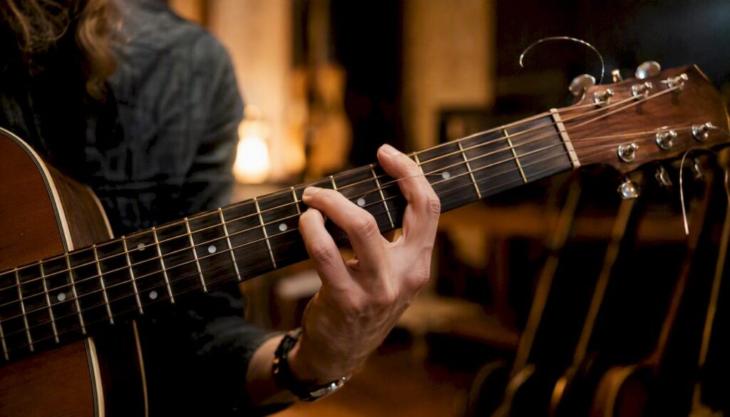 Mit der Hand wird eine Gitarrensaite auf dem Griffbrett gezogen, um den Ton zu verändern.