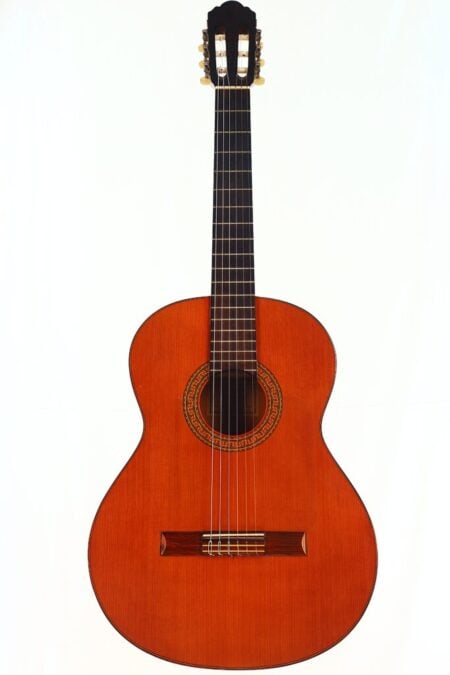 Eine Flamenco-Gitarre von Jose Romero Estudio mit Holzkorpus, sechs Saiten und einer filigranen Rosette um das Schallloch, fotografiert vor einem schlichten weißen Hintergrund.