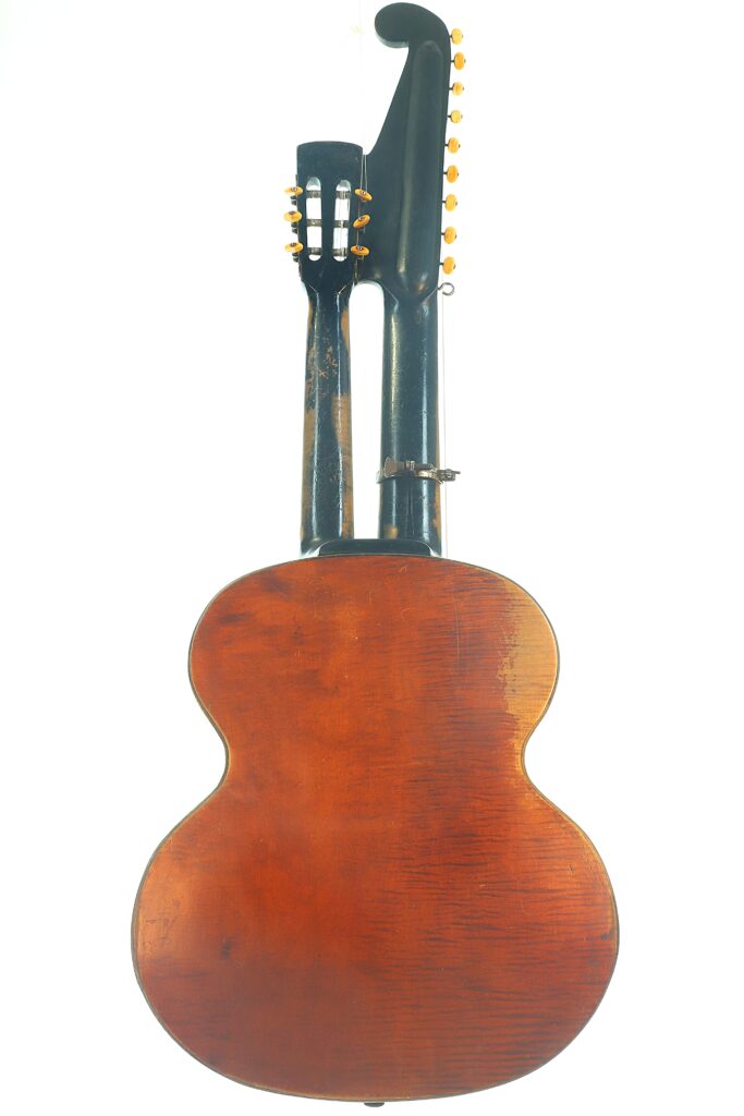 Die Kontragitarre „Gustav Keller Stauffer Stil 1900“ verfügt über einen Holzkorpus mit rotbrauner Lackierung und ist sowohl mit einem Standardhals als auch mit einem zusätzlichen gebogenen Hals ausgestattet, die jeweils mit Stimmwirbeln versehen sind. Sie ist vor einem weißen Hintergrund abgebildet. Die Kontragitarre „Gustav Keller Stauffer Stil 1900“ verfügt über einen Holzkorpus mit rotbrauner Lackierung und ist sowohl mit einem Standardhals als auch mit einem zusätzlichen gebogenen Hals ausgestattet, die jeweils mit Stimmwirbeln versehen sind. Sie ist vor einem weißen Hintergrund abgebildet.