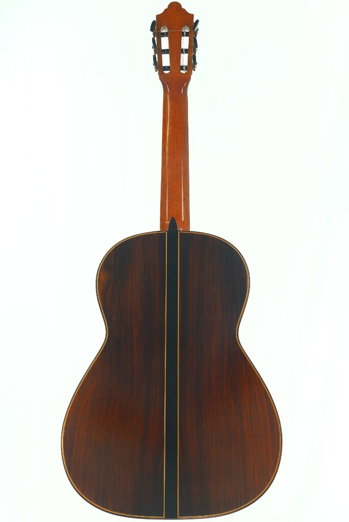 Das Bild zeigt die Rückansicht der „Stefan Nitschke 2015 Friederich Klassische Gitarre“ mit einer Holzoptik, die durch einen dunklen, vertikalen Streifen in der Mitte hervorgehoben wird. Das Bild zeigt die Rückansicht der „Stefan Nitschke 2015 Friederich Klassische Gitarre“ mit einer Holzoptik, die durch einen dunklen, vertikalen Streifen in der Mitte hervorgehoben wird.