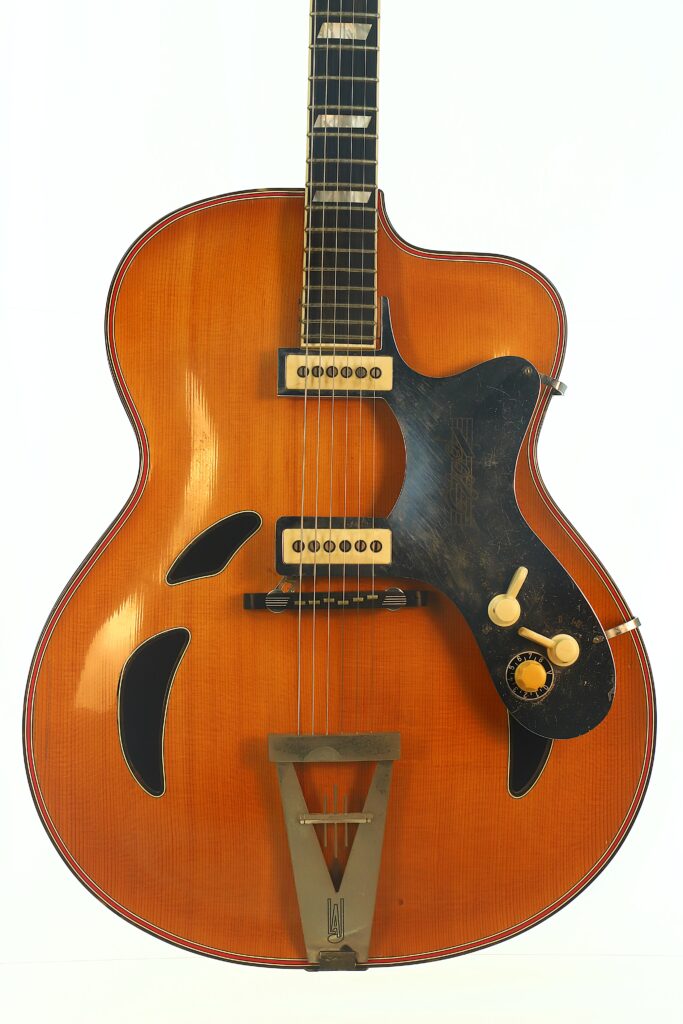 Eine Artur Lang Jazz-Gitarre aus den 1950er Jahren, eine Vintage-Hollow-Body-E-Gitarre mit Sunburst-Lackierung, zwei Tonabnehmern, schwarzem Schlagbrett, drei Reglern und f-förmigen Schalllöchern, abgebildet vor einem schlichten weißen Hintergrund. Eine Artur Lang Jazz-Gitarre aus den 1950er Jahren, eine Vintage-Hollow-Body-E-Gitarre mit Sunburst-Lackierung, zwei Tonabnehmern, schwarzem Schlagbrett, drei Reglern und f-förmigen Schalllöchern, abgebildet vor einem schlichten weißen Hintergrund.