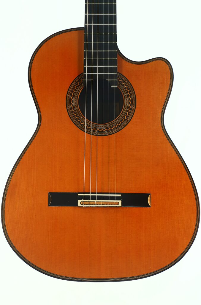 Eine Nahaufnahme der Antonius Müller 2012 Doubletop Klassische Gitarre mit Holzkorpus, aufwendig gearbeiteter Rosette um das Schallloch, schwarzem Steg und Nylonsaiten, abgebildet vor weißem Hintergrund. Eine Nahaufnahme der Antonius Müller 2012 Doubletop Klassische Gitarre mit Holzkorpus, aufwendig gearbeiteter Rosette um das Schallloch, schwarzem Steg und Nylonsaiten, abgebildet vor weißem Hintergrund.