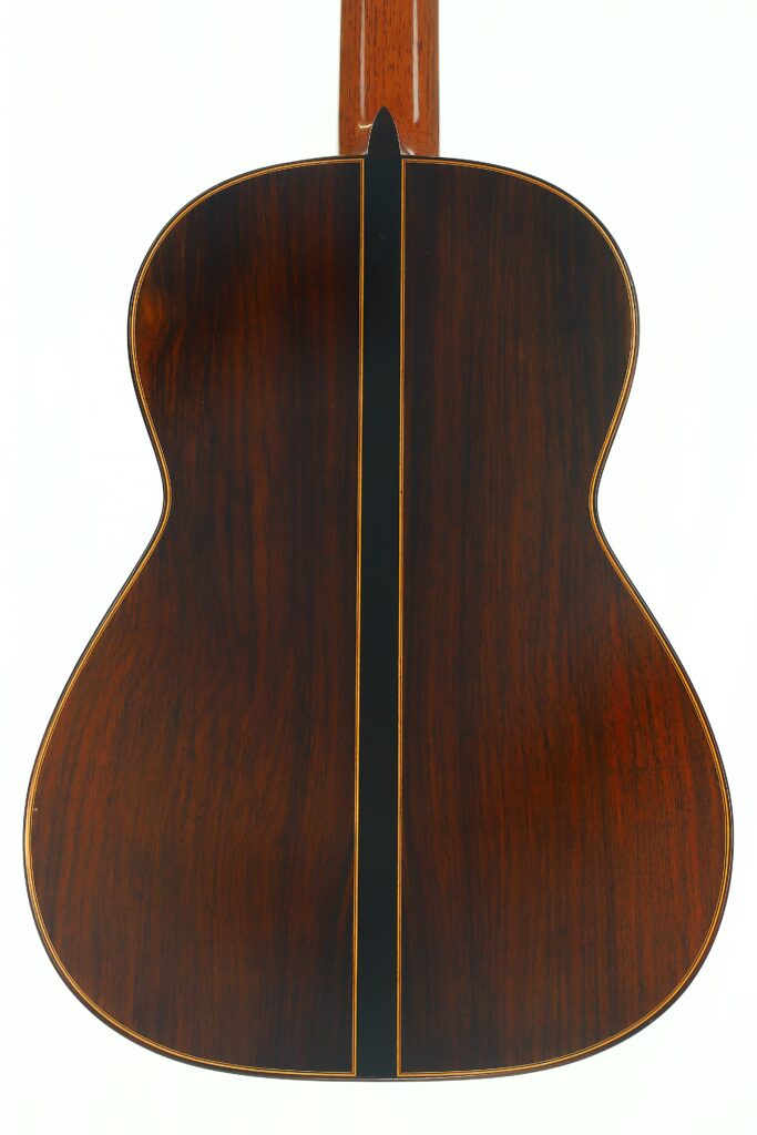 Die Rückseite der „Friederich Klassische Gitarre“ von Stefan Nitschke aus dem Jahr 2015 besticht durch eine dunkle Holzoberfläche mit einem Mittelstreifen und einer sichtbaren Holzmaserung vor weißem Hintergrund. Die Rückseite der „Friederich Klassische Gitarre“ von Stefan Nitschke aus dem Jahr 2015 besticht durch eine dunkle Holzoberfläche mit einem Mittelstreifen und einer sichtbaren Holzmaserung vor weißem Hintergrund.