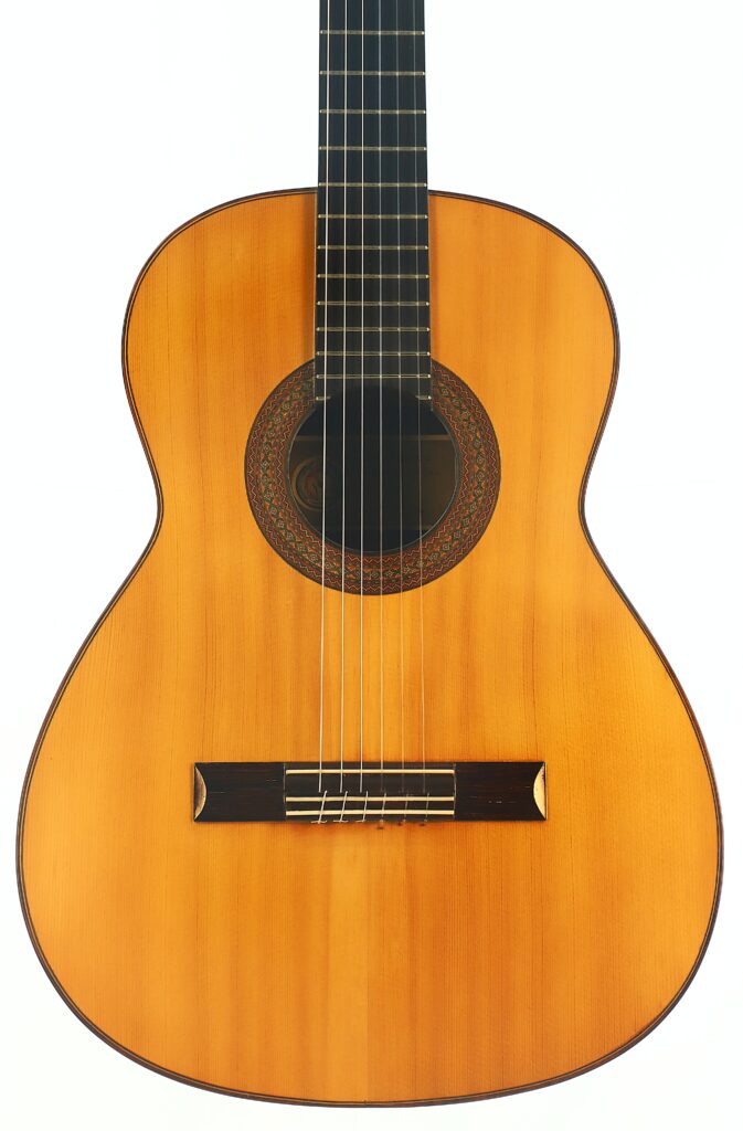 Die „Manuel Adalid Sr. 1971 Francisco Klassische Gitarre“ ist eine klassische Akustikgitarre mit einem Holzkorpus, einem sichtbaren Schallloch mit aufwendig verzierter Rosette und sechs Saiten, die vor einem weißen Hintergrund abgebildet ist. Die „Manuel Adalid Sr. 1971 Francisco Klassische Gitarre“ ist eine klassische Akustikgitarre mit einem Holzkorpus, einem sichtbaren Schallloch mit aufwendig verzierter Rosette und sechs Saiten, die vor einem weißen Hintergrund abgebildet ist.