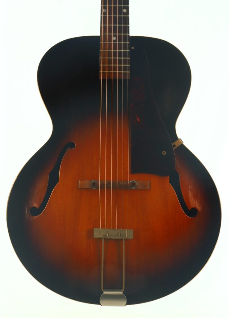Vorderansicht einer Gibson L-48 Akustikgitarre aus dem Jahr 1948, einer Vintage-Archtop-Akustikgitarre mit Sunburst-Lackierung, zwei F-Löchern, sechs Saiten und einem dunklen Schlagbrett vor weißem Hintergrund. Vorderansicht einer Gibson L-48 Akustikgitarre aus dem Jahr 1948, einer Vintage-Archtop-Akustikgitarre mit Sunburst-Lackierung, zwei F-Löchern, sechs Saiten und einem dunklen Schlagbrett vor weißem Hintergrund.